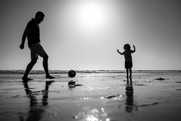 Father and son play soccer or football on the beach on summer family holidays dad and child playing outdoor silhouette on sunset