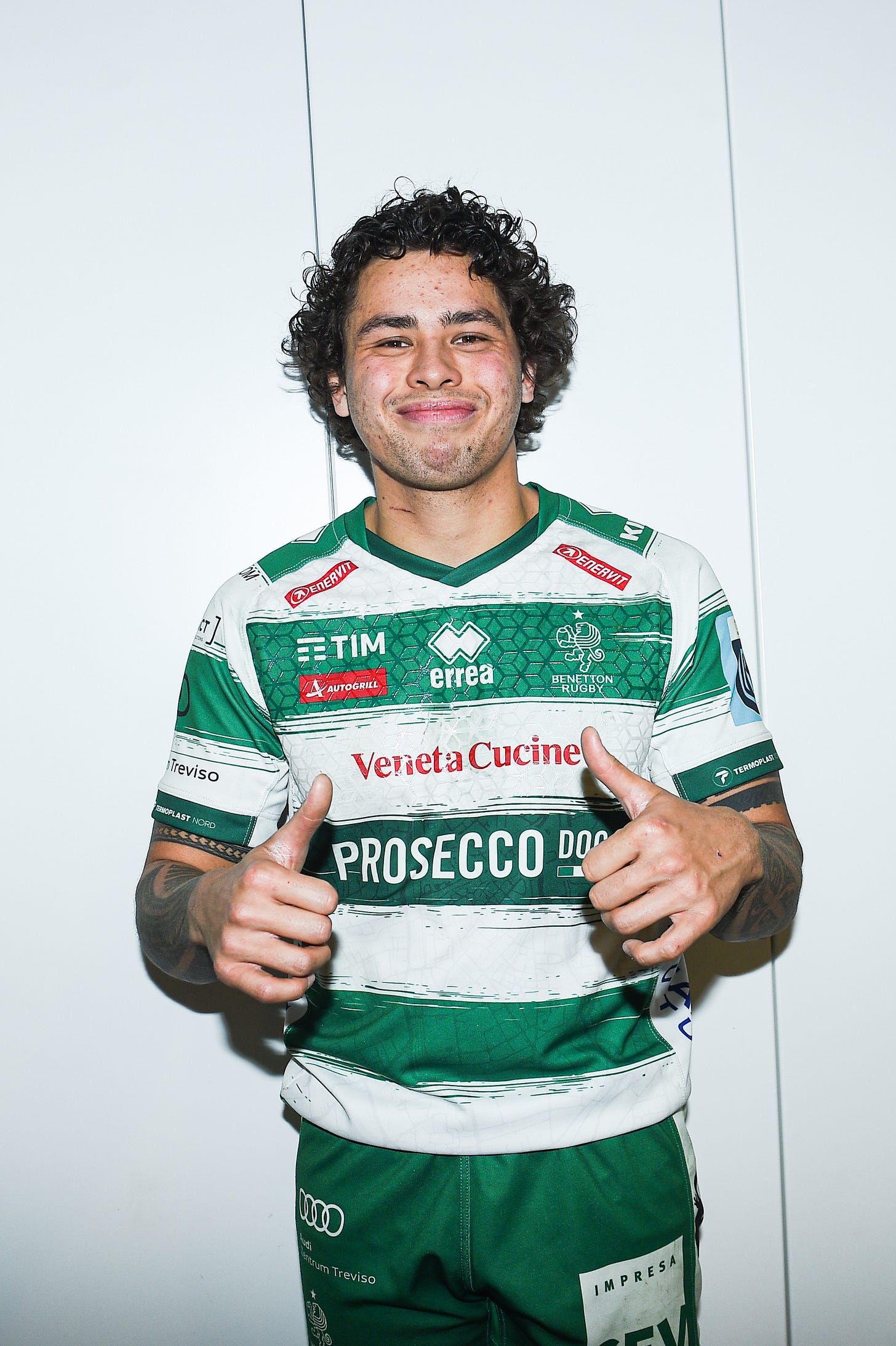 This is an image of a smiling Jacob Umaga after a rugby game, wearing a striped green and white Benetton Treviso rugby jersey, set against a white wall.