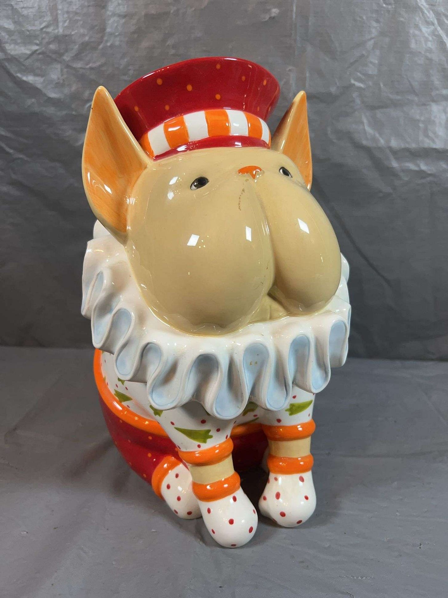 A cookie jar in the shape of a seated French bulldog wearing a jaunty cap with a big 17th-century sort of ruffle... but also there's lots of polka dots and evergreen trees?