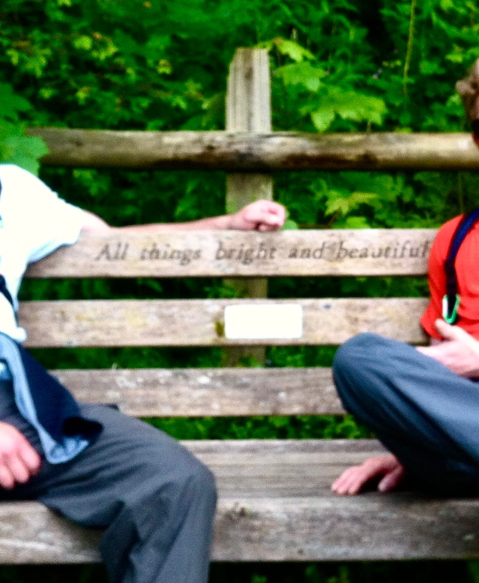 The arms of two figures on a bench showing the sign 'All things bright and beautiful'