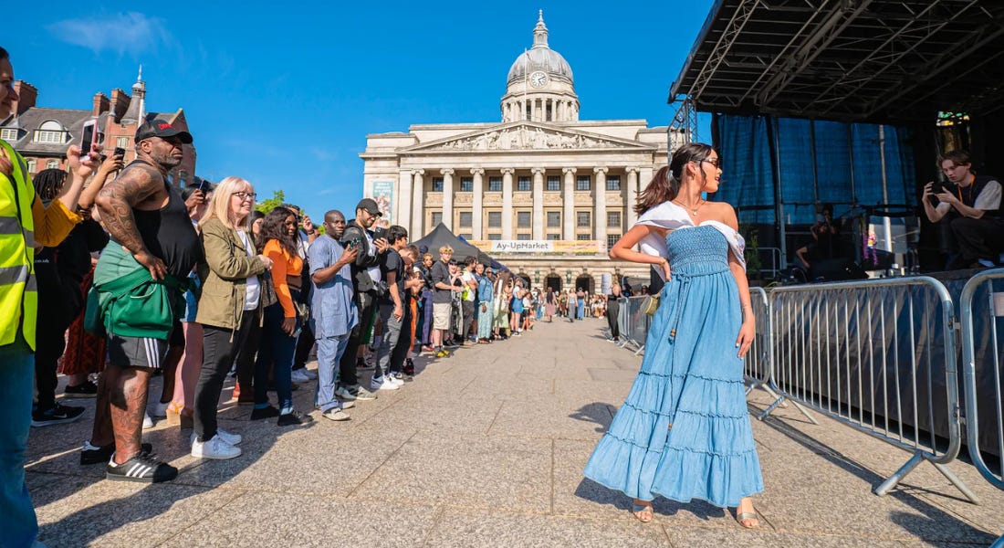 A girl posing in a blue dress, with a crowd to the left of her and photographers to the right of her