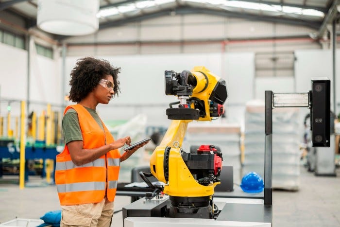Female engineer uses a digital tablet to program and control a robotic arm inside a modern factory