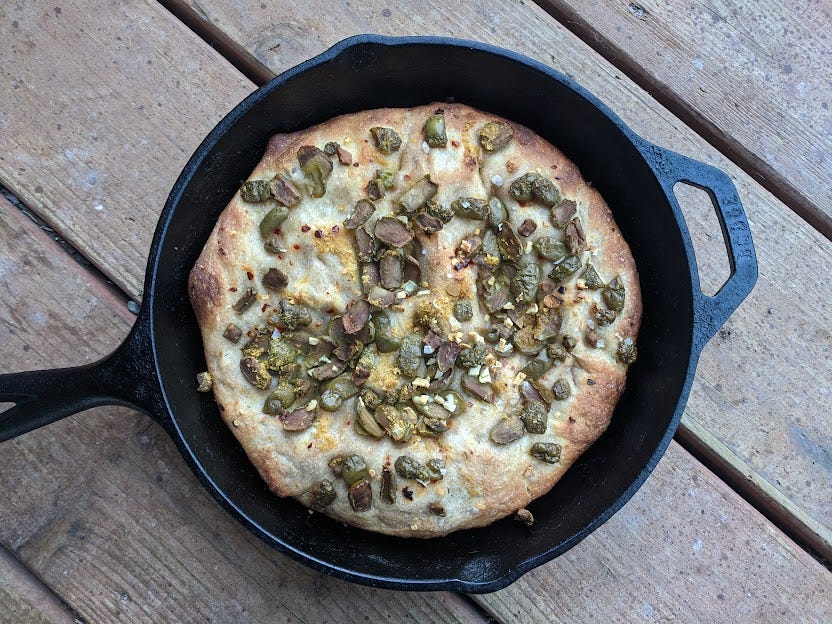 a round cast iron pan of olive adorned focaccia