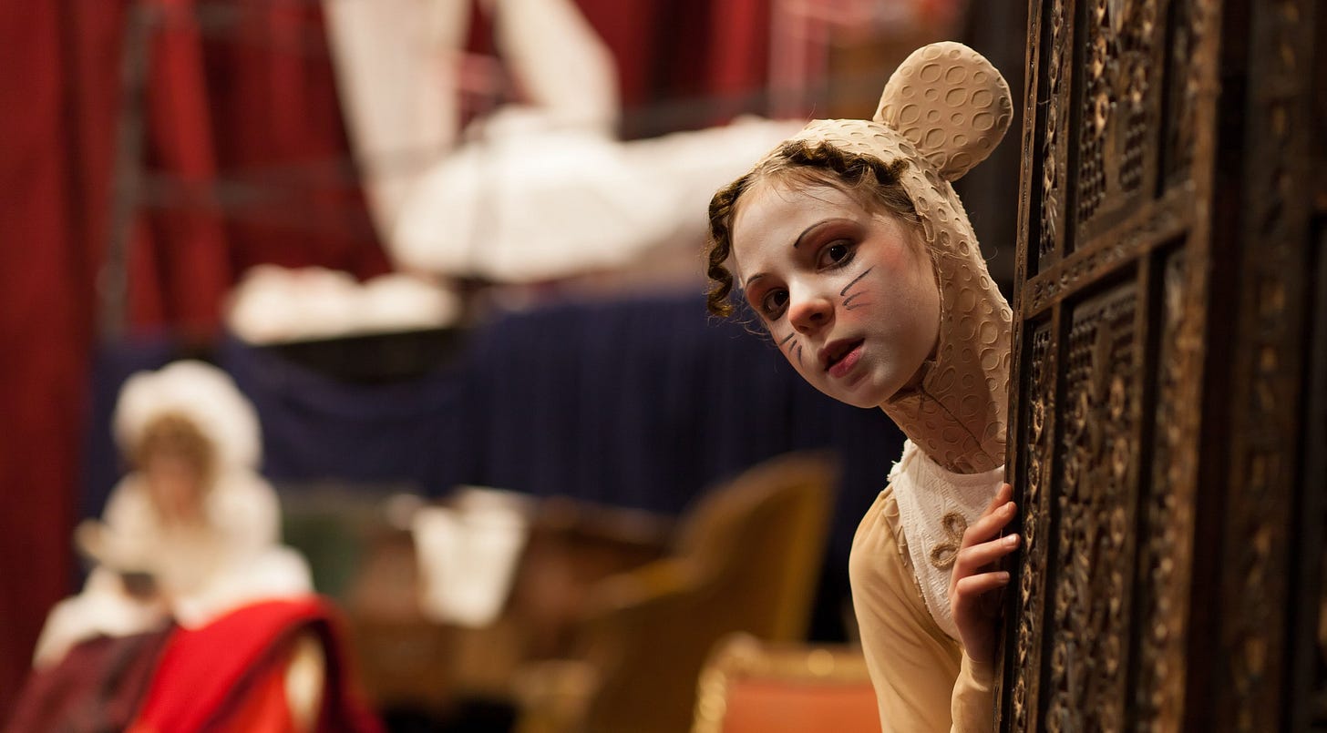 A young actress, dressed as a mouse, peeks from behind a wall.