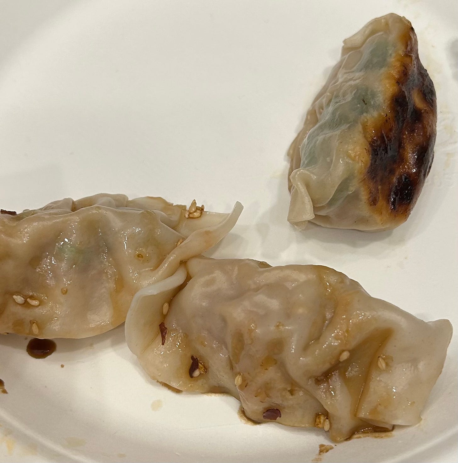 Three dumplings on a paper plate, two boiled and dressed in a soy sauce mixture on the bottom and one pan-fried one toward the top left
