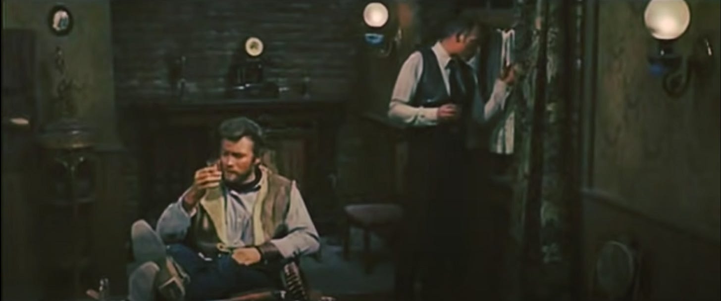A frame from For a Few Dollars More, with Manco and Mortimer sharing a drink. Manco has his feet kicked up examining his glass, and Mortimer is peering sidelong out the window.