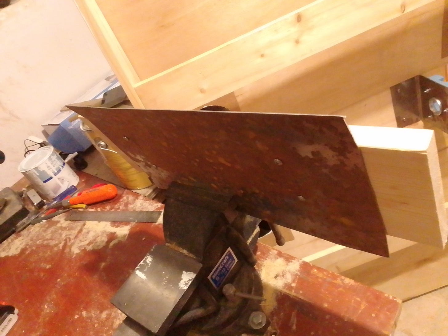 Metal plate screwed to a 1x6 with the edge in a vice, undergoing precision bending process... with a hammer