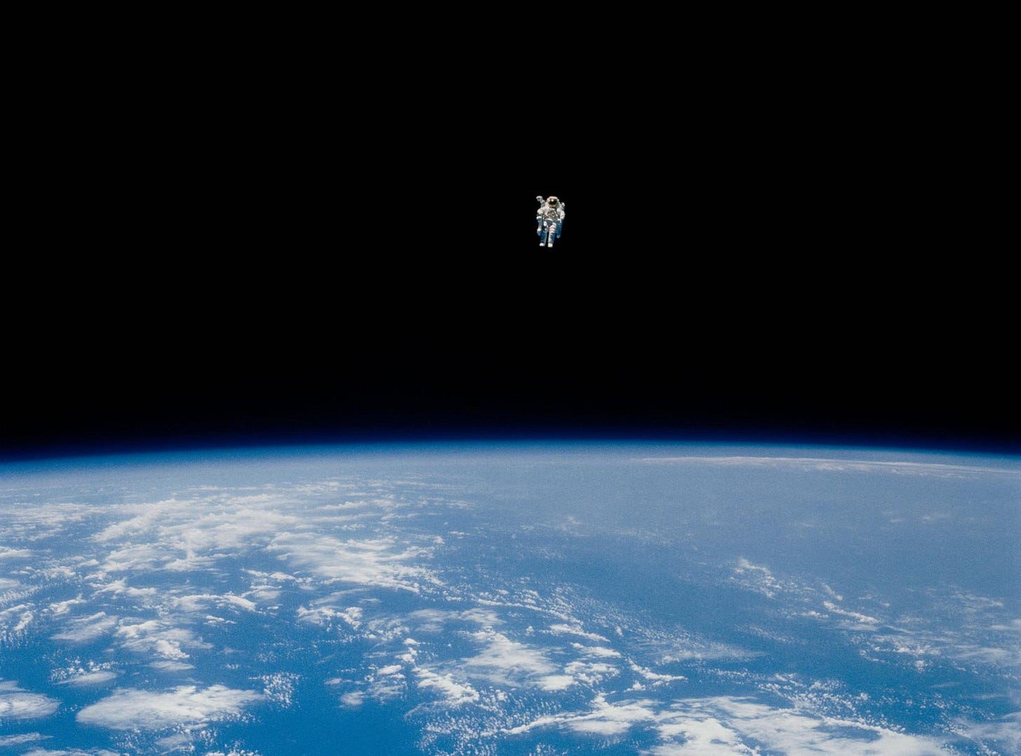 An astronaut in a spacesuit floats alone above Earth, with the planet's blue surface and clouds visible below against the blackness of space—an image capturing humanity’s quest for discovery.