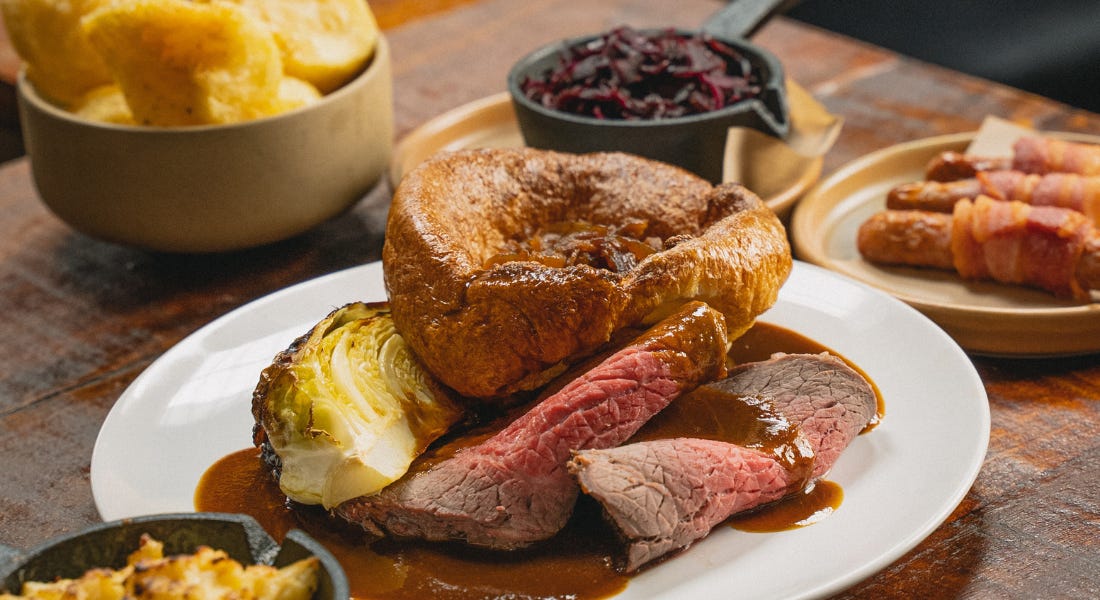A close-up of a Sunday roast with a yorkshire pudding, beef, and cabbage on it A close-up of a Sunday roast with a yorkshire pudding, beef, and cabbage on it