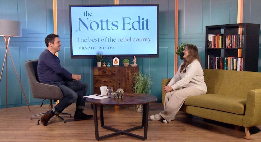 Two people sat on chairs on a TV set with a TV screen above it