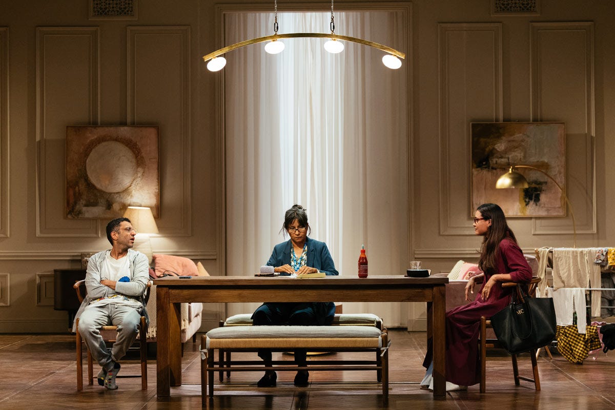 Adeel Akhtar as Angad and Thusitha Jayasundera and Shelley Conn as Gyan and Malicka sit around a table in his swanky flat.