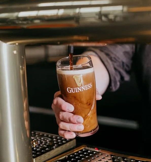 This may contain: a person holding a drink in their hand and pouring it into a glass with the word guinness on it