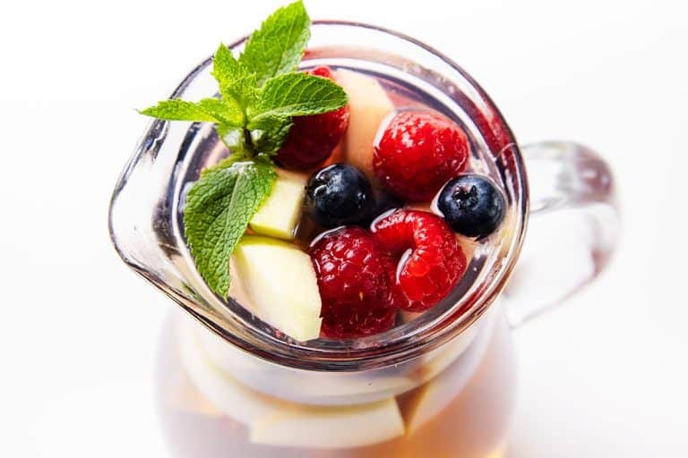 Pitcher of homemade white sangria filled with fresh raspberries, blueberries, apple slices, and mint.