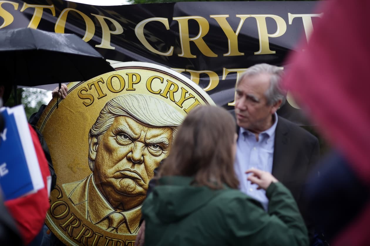 Protesters with signs, one depicting a stern Donald Trump, outside Trump National Golf Club.