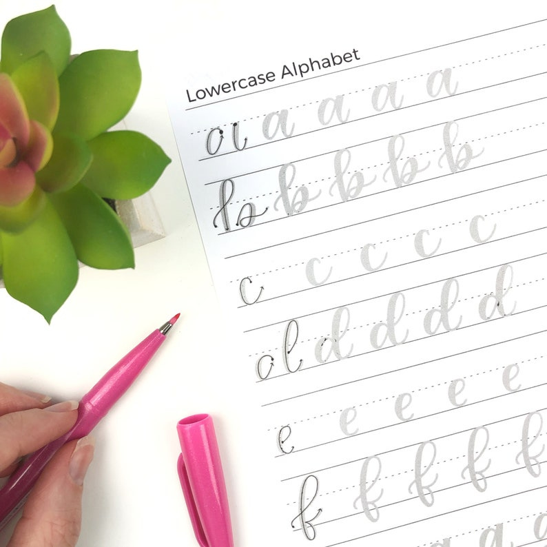 May include: A lowercase alphabet practice sheet with gray lines and gray letters. The letters are written in cursive. The sheet is on a white surface.