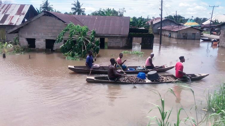 People paddle canoes down a flooded residential street past half-submerged residential houses. People paddle canoes down a flooded residential street past half-submerged residential houses.