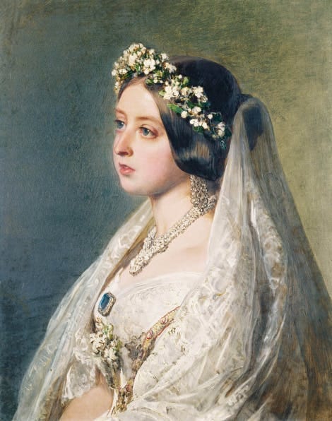 Close up portrait of a woman facing off to the side wearing a flower crown and a veil wearing a dress.