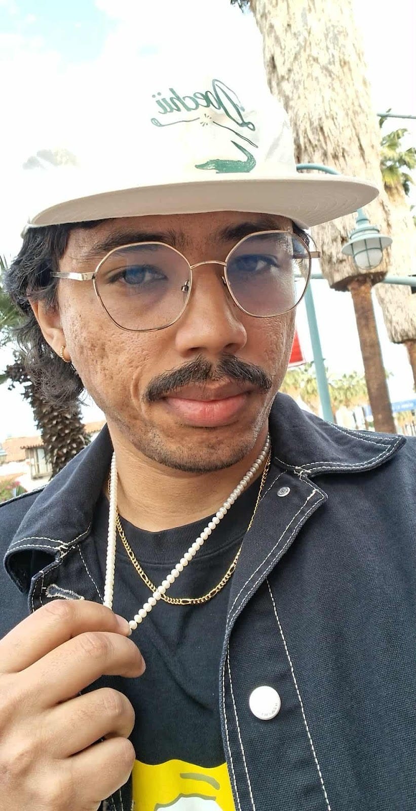 Selfie of me, holding my necklace. I have an unimpressed look on my face.