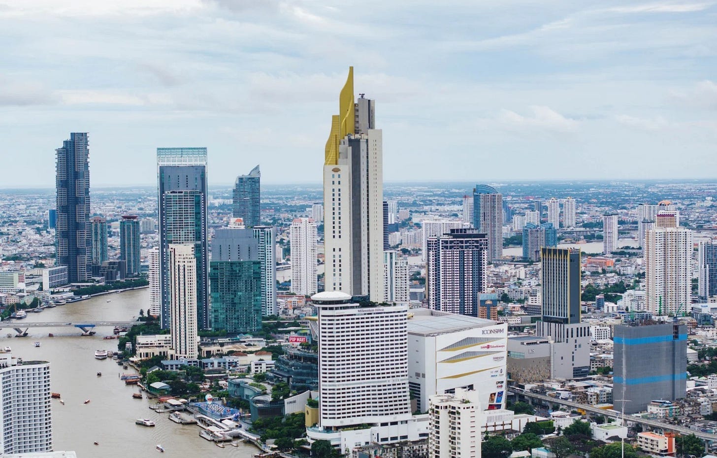 Aerial view of Bangkok's Chao Phraya River lined with high-rise condominium towers and the ICONSIAM complex under an overcast sky. Aerial view of Bangkok's Chao Phraya River lined with high-rise condominium towers and the ICONSIAM complex under an overcast sky.