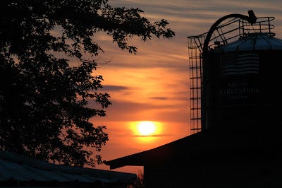 The sun sets behind the silo at the farm
