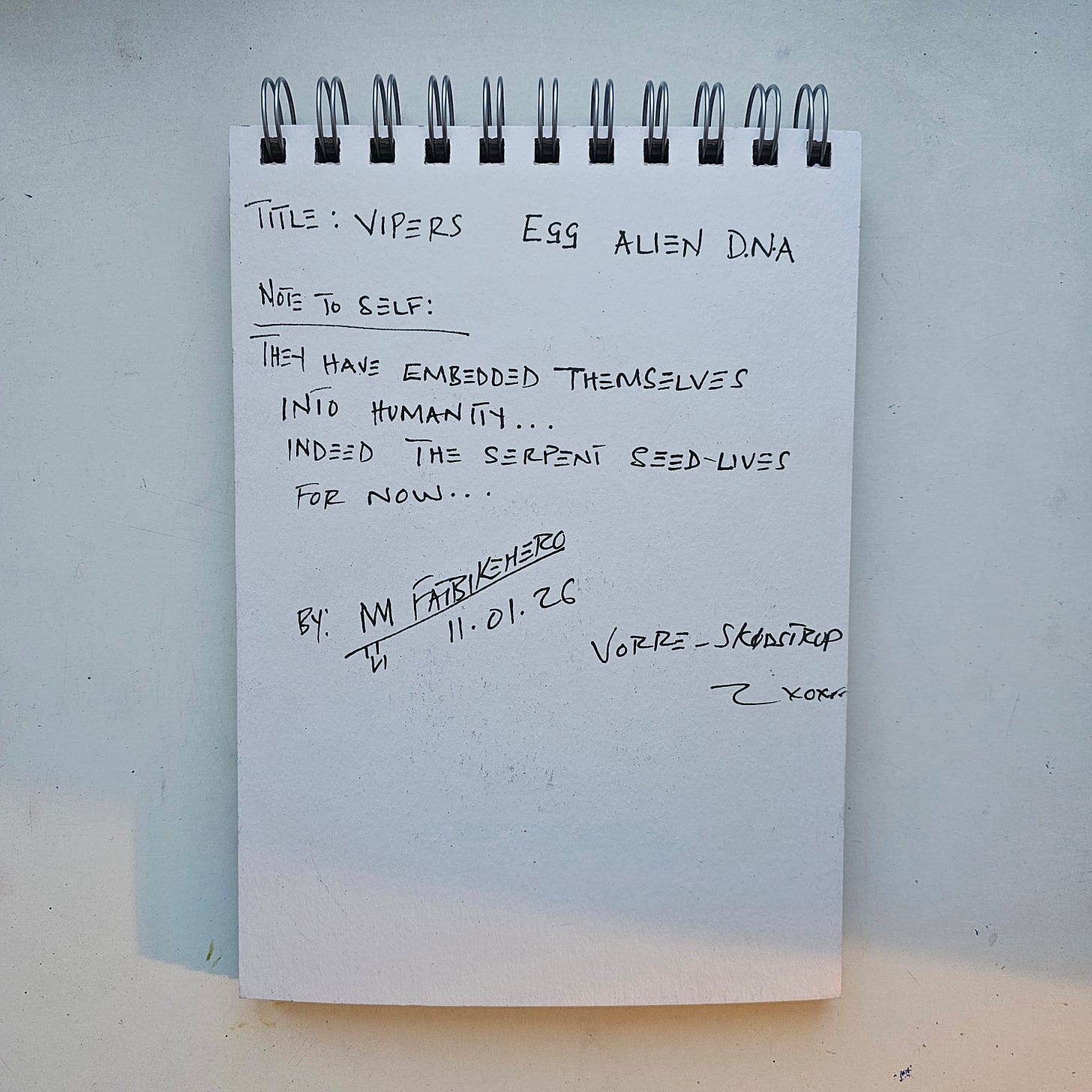 Alt Text:  A photograph of a handwritten note in a spiral notebook by artist FatbikeHero. The text reads "TITLE: VIPERS EGG ALIEN D.N.A" and "NOTE TO SELF: THEY HAVE EMBEDDED THEMSELVES INTO HUMANITY... INDEED THE SERPENT SEED LIVES FOR NOW..." Signed FatbikeHero, dated 11.01.26, location Vorre-Skødstrup.