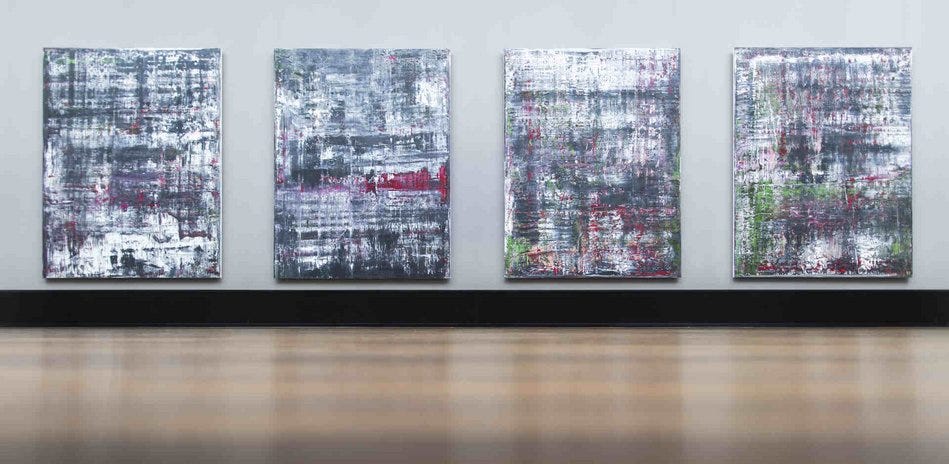 Quatro telas grandes na vertical de pinturas abstratas com a cor cinza se sobressaindo. Elas estão na parede e não há ninguém na frente delas.