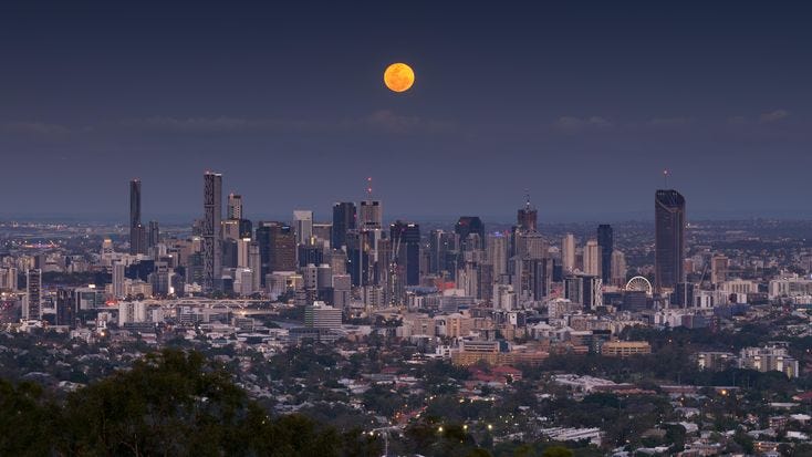 This may contain: the full moon is seen over a city skyline in this view from atop a hill