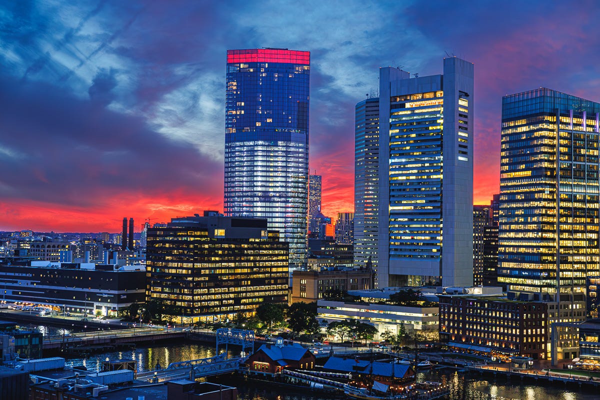Boston Seaport skyline glowing under vivid red-orange sunset light seen from 14th-floor balcony.