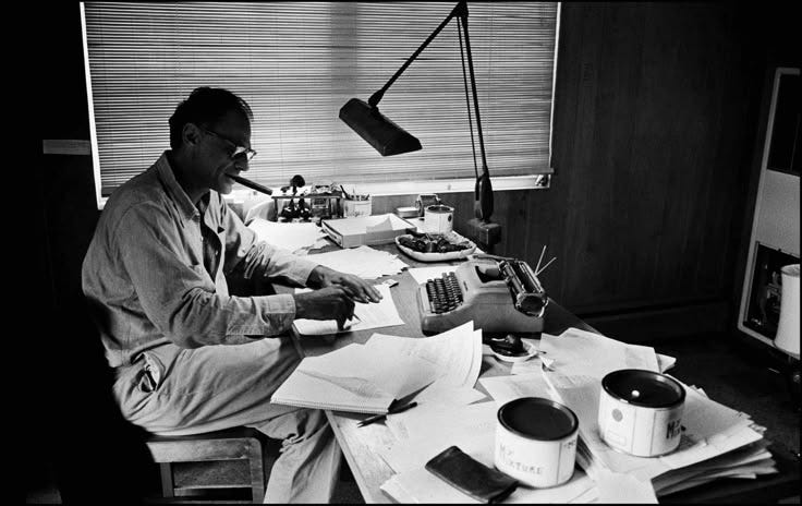 This may contain: a man sitting at a desk in front of a typewriter with papers on it