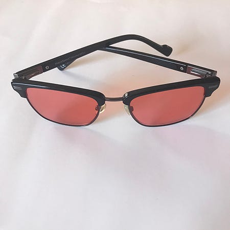 A still photo of Rachel Cassandra’s migraine glasses, red-brown lens with black frames on a white background.