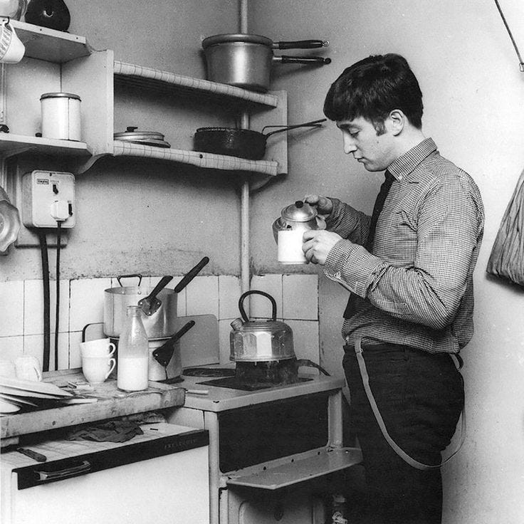 This may contain: an old photo of a man in the kitchen drinking from a cup and pouring milk
