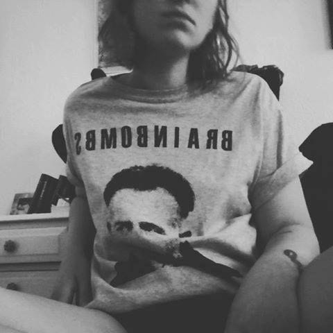 This may contain: black and white photograph of a woman sitting on a bed wearing a t - shirt that says brain bomb