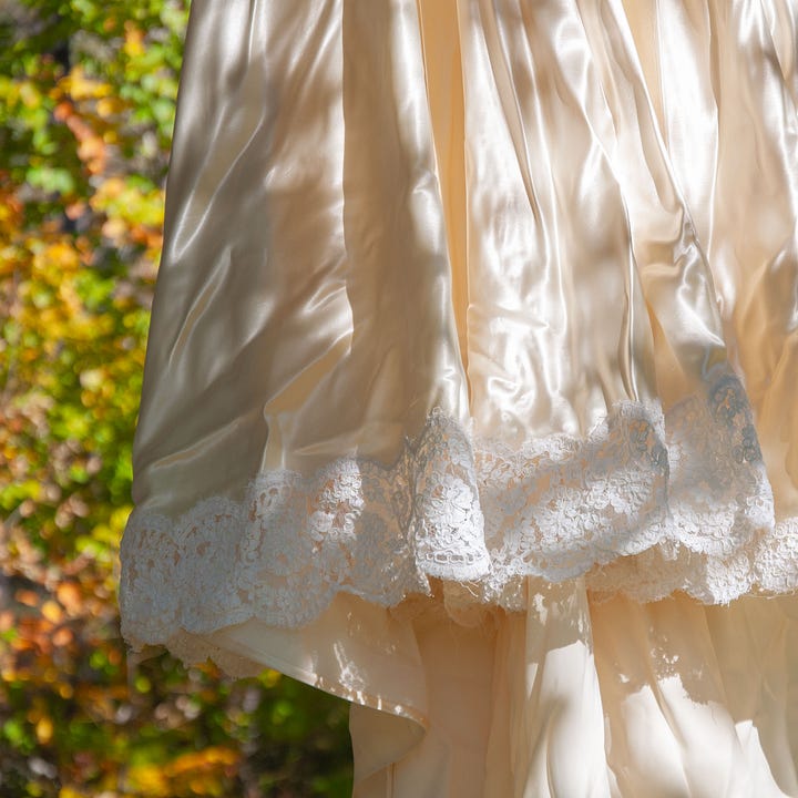 Diptych: Bottom skirt of a satin dress with lace around the border and fall trees blurred behind; Right: Double exposure, red and orange leaves on grass covered by the translucent wrinkles of the same dress.