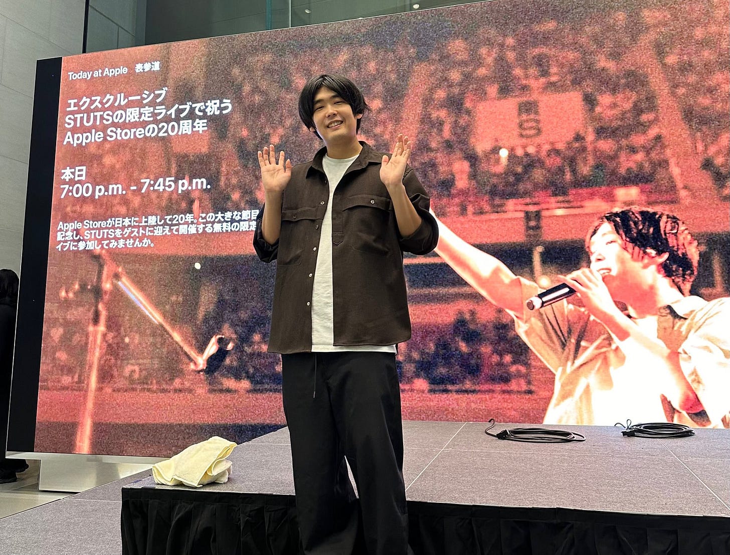 Artist STUTS waves in front of the video wall at Apple Omotesando.