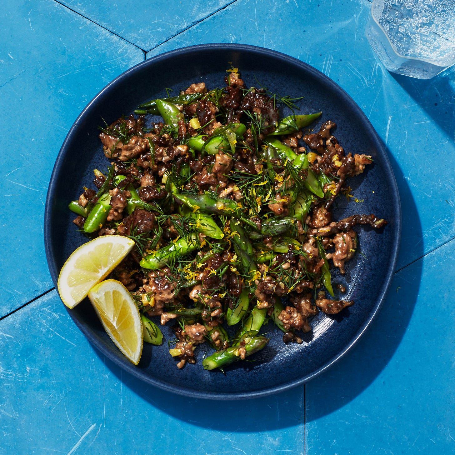 Dark bowl of lamb stir fry on bright blue tiles.