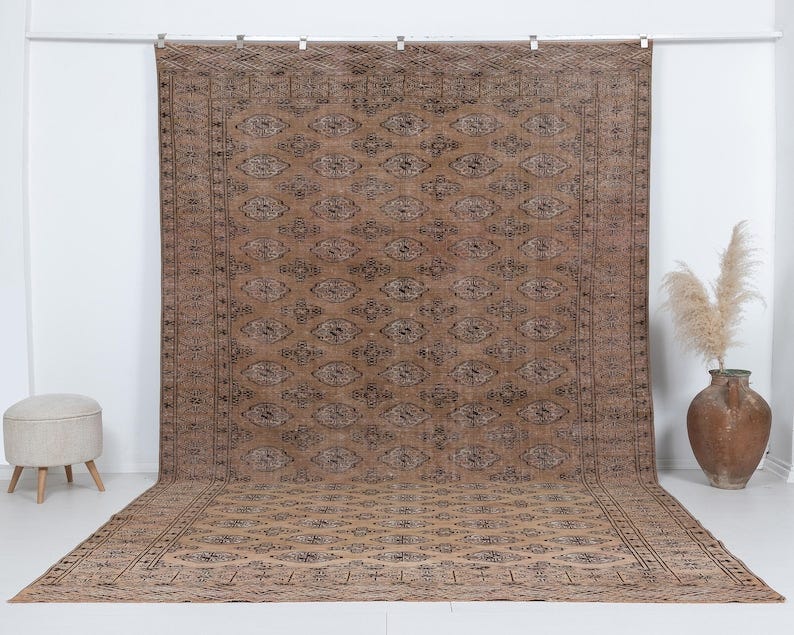 May include: A brown and black patterned rug with a geometric design. The rug has a fringe border and is hanging on a white wall.
