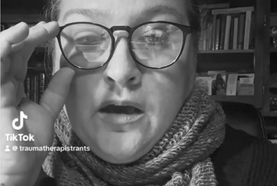 Alt Text: Dr. Jamie wears glasses, a tight scarf and giving a snotty look in her uppity therapy character on TikTok