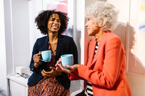 Free Two diverse women enjoying coffee together in a modern office setting. Stock Photo