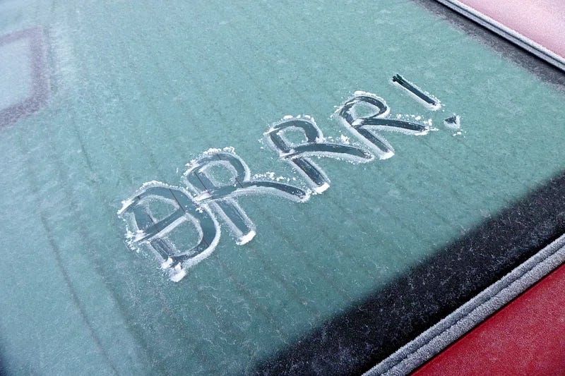 Frosted over back window of a car with the word BRRR! carved into the frost with a finger.