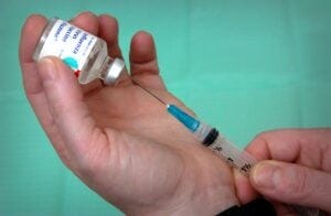 a vaccine vile with a needle pulling fluid from it