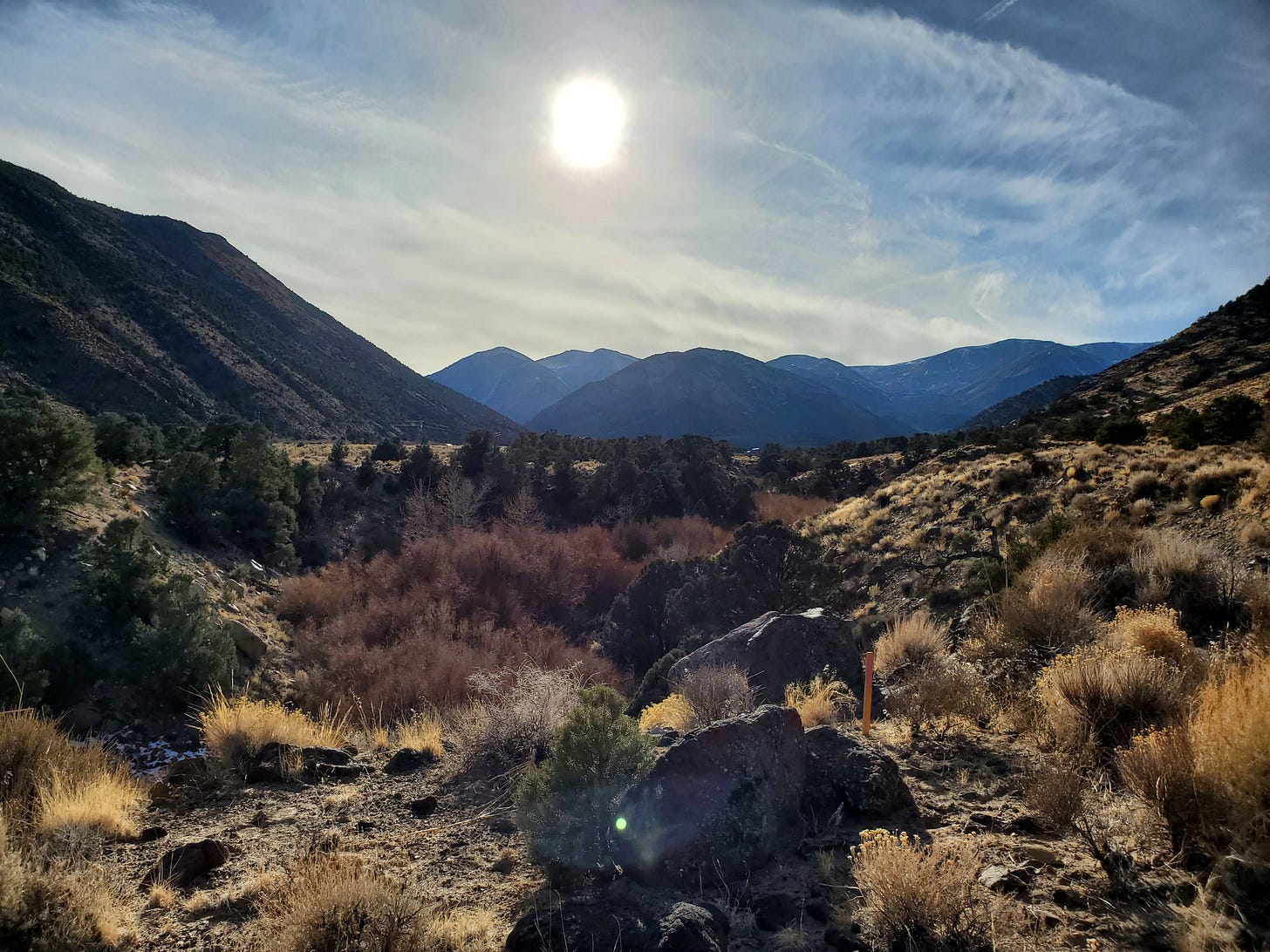 View of valley and hillsides on the left and right with White Mountains in distance and sun setting.