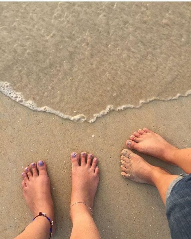 Waves approaching two people's feet. The feet are covered in mud. 