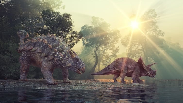 Two plant-eating dinosaurs pause at a watering hole. Two plant-eating dinosaurs pause at a watering hole.