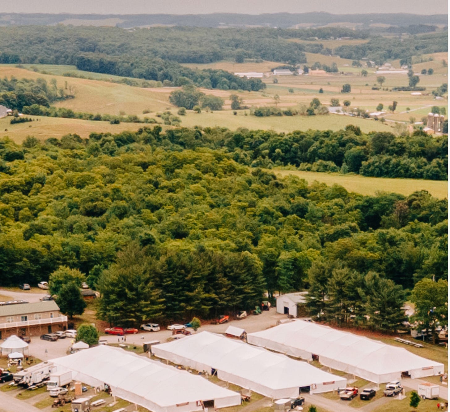 Aerial view of white event tents among rolling green wooded hills and farmland. Aerial view of white event tents among rolling green wooded hills and farmland.