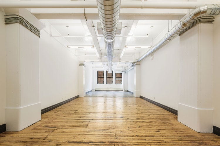 an empty industrial space with both wood and concrete floors and blank white walls
