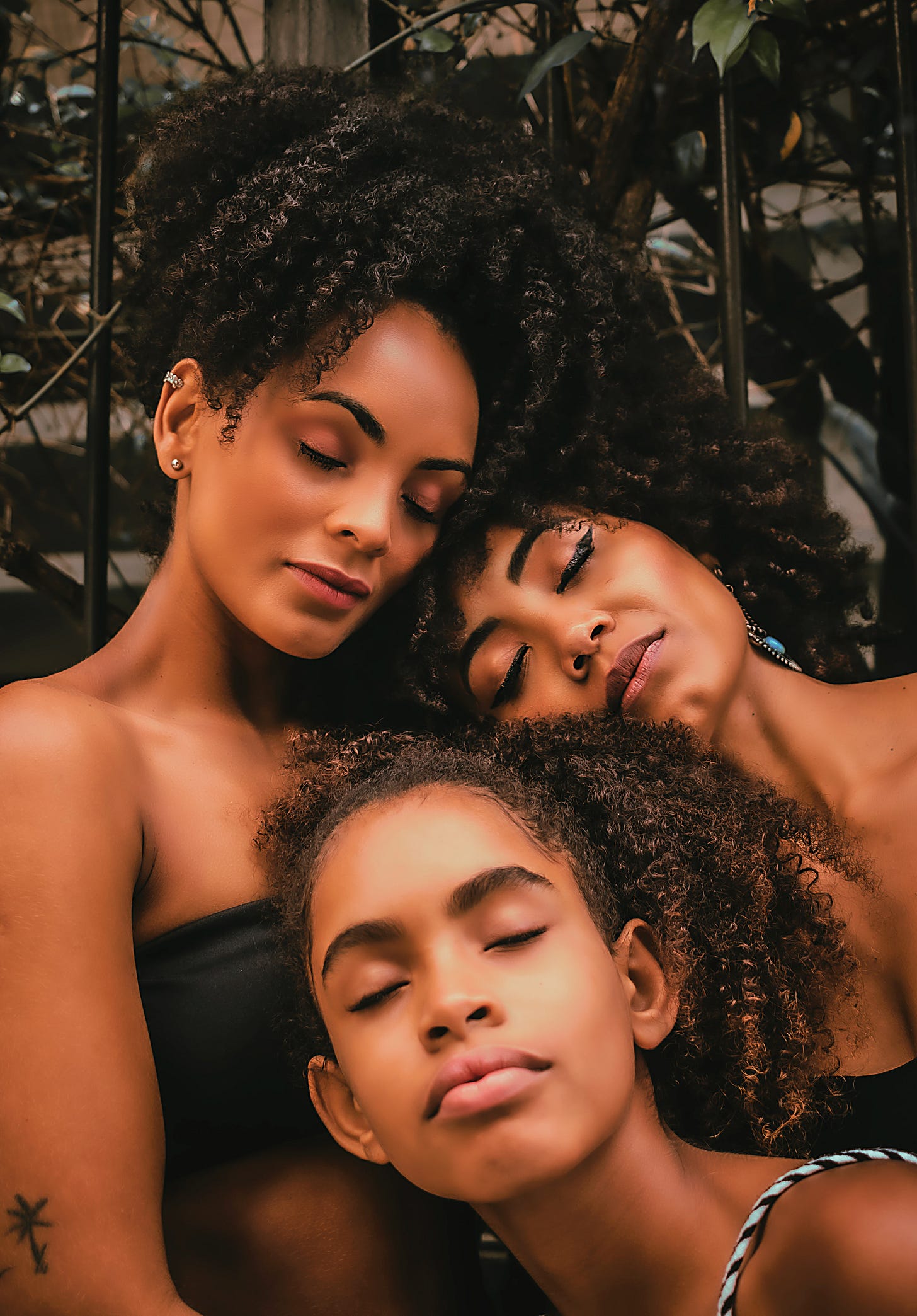 Three woman with curly hair, closing their eyes and laying their head on each other Three woman with curly hair, closing their eyes and laying their head on each other