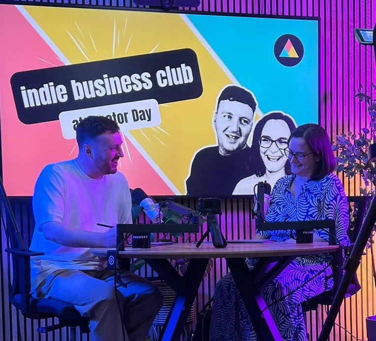 Mel and Ben recording in a beautifully lit studio with indie business club branding behind us