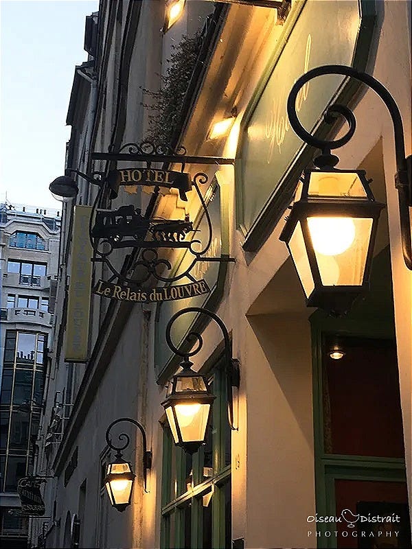 Hotel shop front with yellowish lit street lamp, a dawn sky backdrop in Paris.