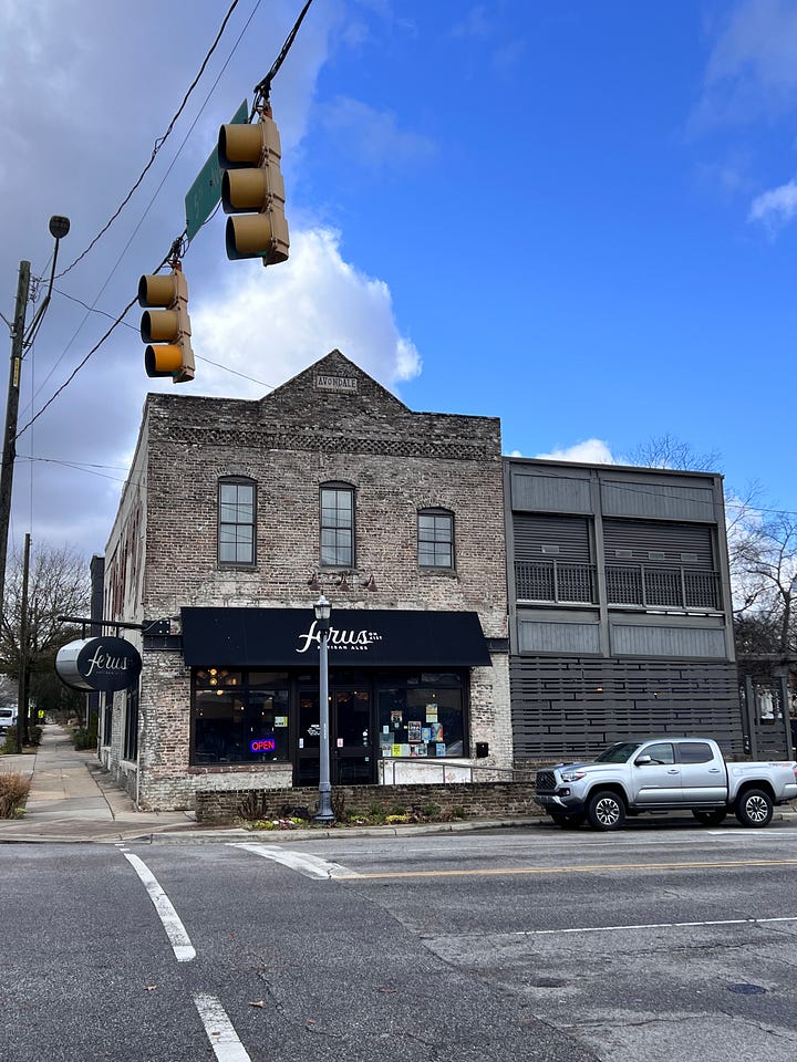 a brick building on a corner with blue skies behind it and a metal sign on a brick wall that says Avondale Common House
