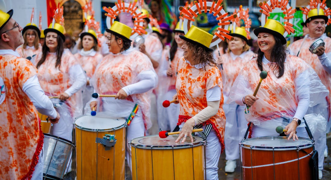 A grop of people wearing white outfits and yellow hats banging samba drums A grop of people wearing white outfits and yellow hats banging samba drums